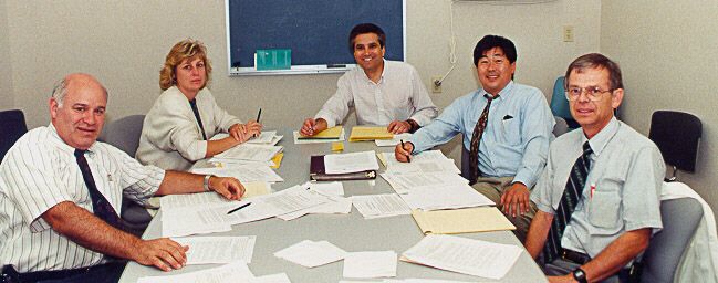 people seated at conference table with many scattered papers.
