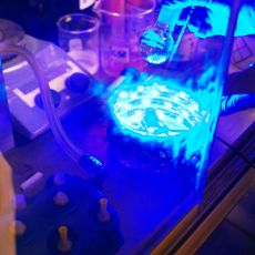 a hand holds an object while blue light illuminates scientific equipment.