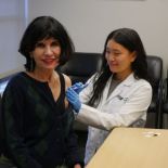 Pharmacy student in white coat administers flu shot to dean