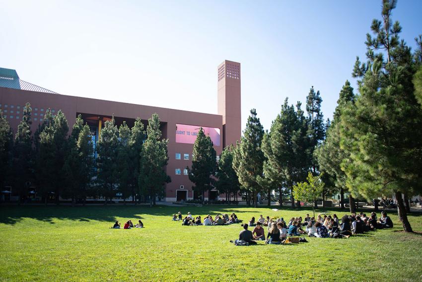 People sit on a lawn in a quad in a university setting