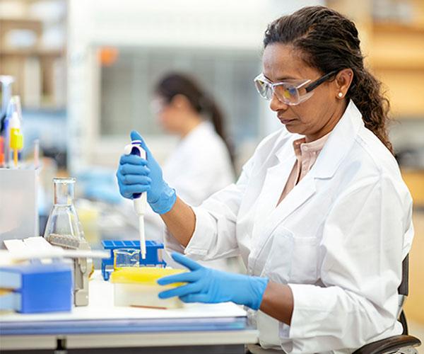 woman in white lab coat uses a pipet in a research lab