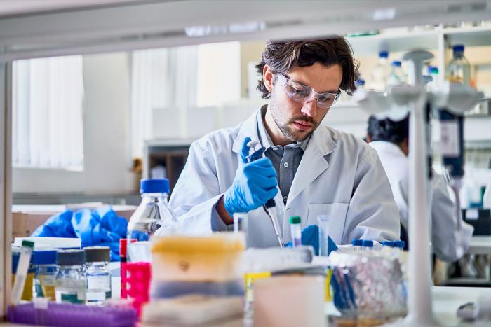 researcher in white lab coat uses pipet in research lab