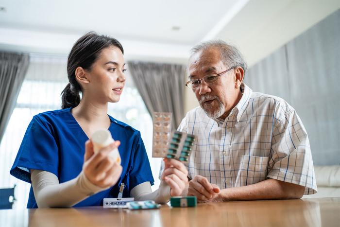 health care worker in scrubs holds medication and advises a senior patient