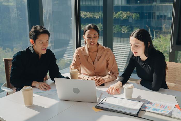 three people have a discussion while reviewing info on a laptop